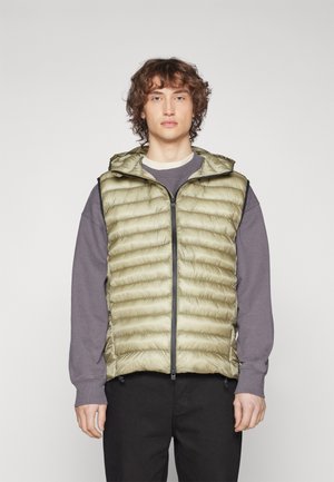 Lyse olivengrønn puffervest med quiltet design, hel glidelås og hette; brukt over en grå hettegenser med svarte detaljer og lommer.