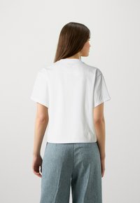 T-shirt en coton blanc à manches courtes, design court et décolleté rond. Porté avec un pantalon large texturé bleu clair.