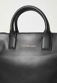 Must have nahkakott, millel on kaks ümarat sangad, esiosas on kullavärvi "TOMMY HILFIGER" logo ja tekstureeritud pind.