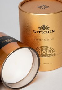 Candela color oro con una finitura metallica, etichettata "Wittchen Secret Passion," con una banda di accento nera e un interno in cera bianca liscia.
