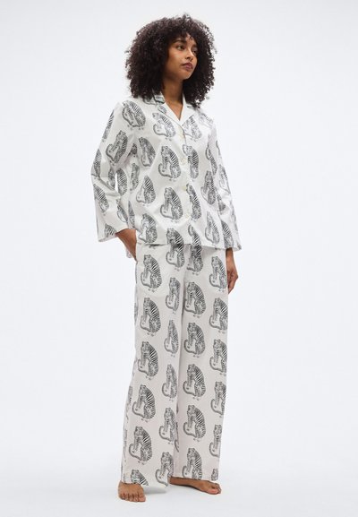Λευκή πιτζάμα με μοτίβο μαύρης τίγρης. Πουκάμισο με κουμπιά και μακριά μανίκια και παντελόνια με φαρδύ πόδι. Λεία υφή υφάσματος με άνετη εφαρμ ογή.