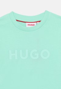 Πράσινο-μέντα βαμβακερό t-shirt με στρογγυλή λαιμόκοψη και διακριτικό ανάγλυφο λογότυπο "HUGO" στο μπροστινό μέρος. Διαθέτει ετικέτα σε αντίθετο κόκκινο χρώμα στο εσωτερικό.