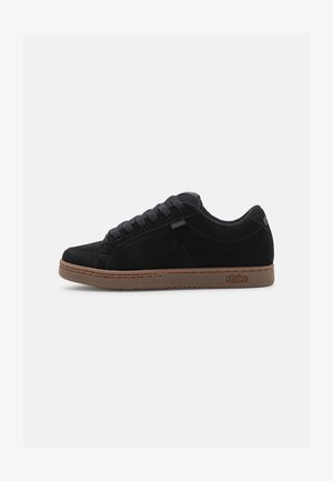 Zapatillas de ante negro con paneles laterales perforados, puntera redondeada y suela de goma marrón. Incluye cordones negros y un diseño sutil de marca.