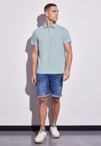 Svetle modrá polo košile s límečkem, v kombinaci s ohrnutými džínovými šortkami. Bílé tenisky se zelenými akcenty. Minimalistický design, hladká látka.