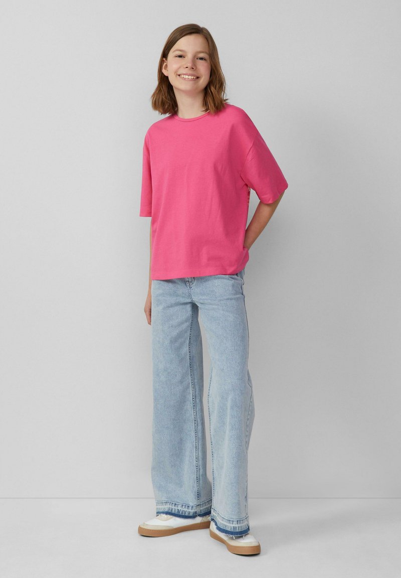 Roze t-shirt met korte mouwen, relaxte pasvorm, gecombineerd met lichtblauwe wijde jeans. Informele schoenen in wit en bruin. Eenvoudig ontwerp.