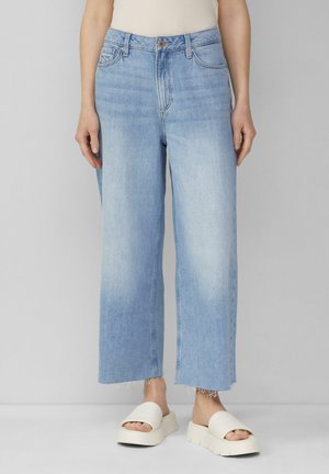 Jeans en denim de couleur bleu clair à jambes larges, dotés d'une taille haute, d'une fermeture à bouton et d'ourlets bruts. Associés à des sandales à plateforme blanches.