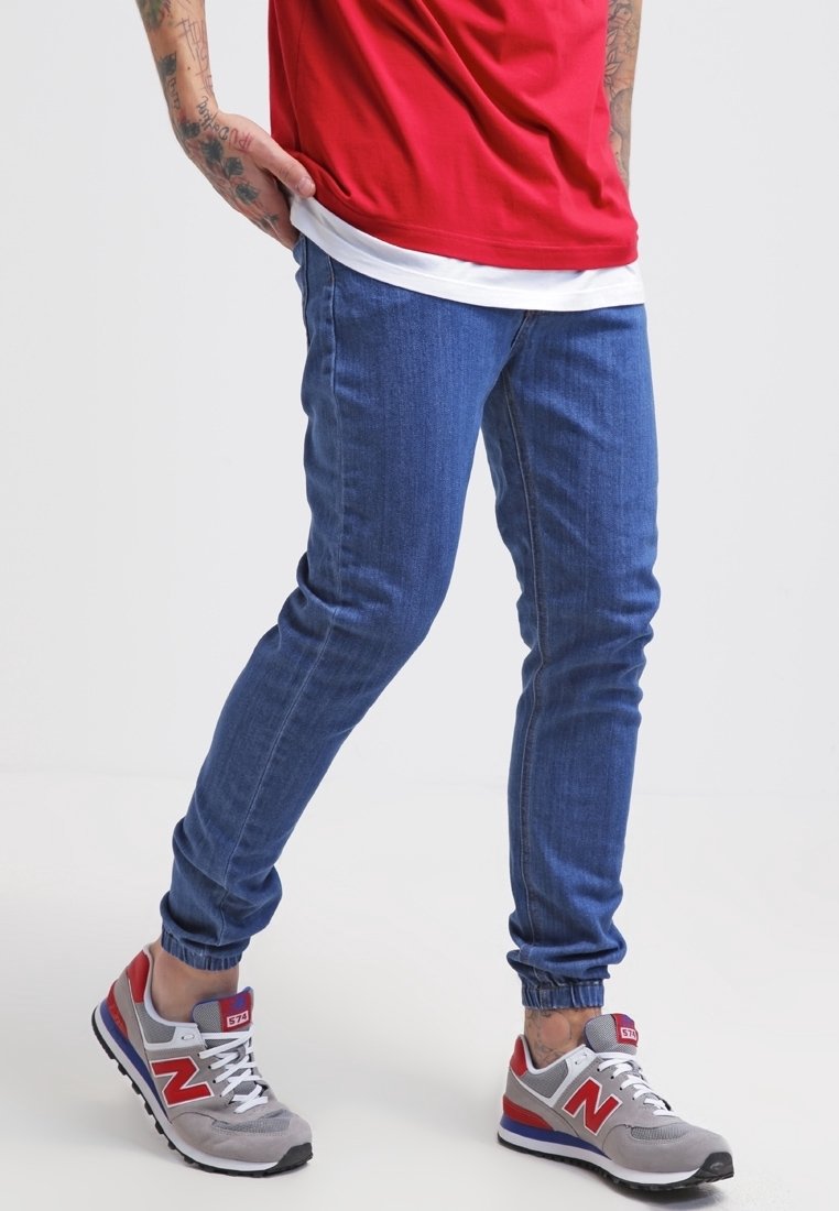 Jeans-joggers i medelblått, med en tapered passform, elastiska muddar och subtila sömnadsdetaljer. Matchas med gråa och röda sneakers.