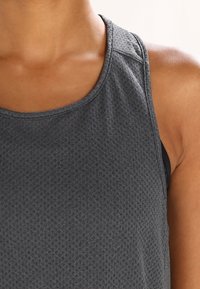 Canotta atletica grigia con tessuto testurizzato, scollatura arrotondata e design senza maniche. Include uno strato interno di reggiseno nero per il supporto.