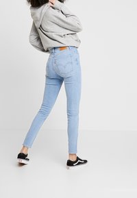 Vaqueros ajustados de color azul claro con cintura alta, que cuentan con un parche de cuero en la parte posterior, combinados con una sudadera gris y zapatillas negras.