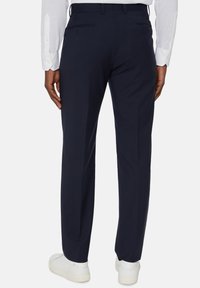 Marinblå byxor i ett glatt tyg, med en skräddarsydd passform, subtila bakfickor och en ren midja. Bärs med vita sneakers.