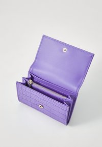 Portafoglio viola con una texture a motivo coccodrillo, dotato di chiusura a scatto e una tasca con zip. L'interno è liscio e di un viola coordinato.