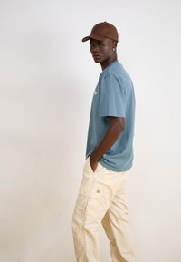 Light blue cotton t-shirt with a crew neck, paired with beige cargo pants featuring multiple pockets, and a brown cap. Simple, unembellished design.
