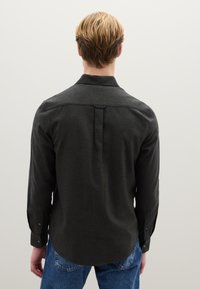 Donkergrijs shirt met lange mouwen, voorzien van een knoopkraag, een achterplooi en knoopmanchetten, gecombineerd met een blauwe spijkerbroek. Gladde textuur en een casual pasvorm.