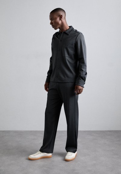 Tumedat hallid nööbid shirt, millel on tekstureeritud muster, koos sobivate kohandatud pükstega ja valgete tossudega, millel on heleda pruunid tallad.