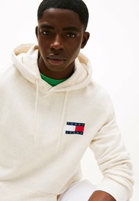 Felpa color crema realizzata in morbido tessuto, con un piccolo logo con elementi blu, rossi e bianchi sulla parte sinistra del petto.