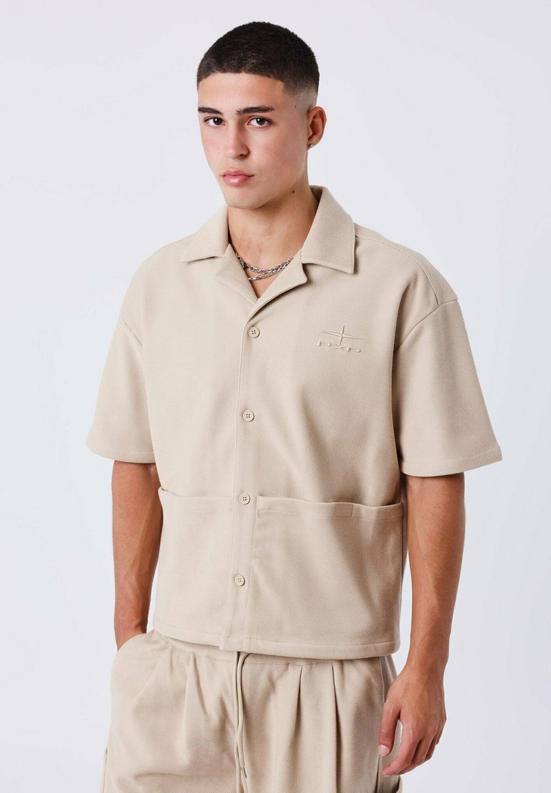 Beige short-sleeve button-up shirt met een relaxed fit, gestructureerde stof en een borstzak. Logo geborduurd op de borst.