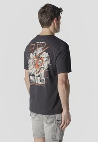 Man wearing black T-shirt with large colorful tiger graphic and "WILD" text on back, paired with light gray shorts, facing away.