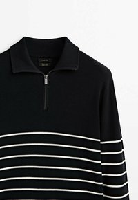 Pull en maille noire avec un col zippé et des rayures blanches horizontales sur la poitrine et les manches.