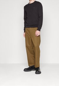 Maglione nero a maglia con scollo rotondo, abbinato a pantaloni larghi color verde oliva. Stivaletti neri completano l'outfit.