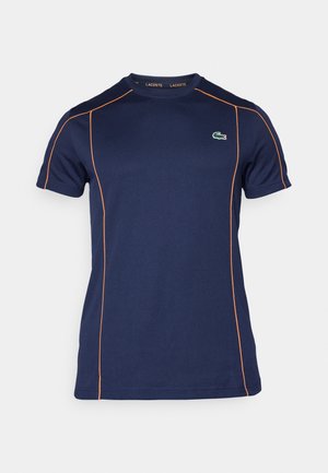 Camiseta navy para hombres hecha de tela suave con detalles de costura en color naranja. Presenta un cuello redondo y un logo de cocodrilo verde en el pecho.