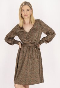 Rochie tip envelopă din material verde închis cu un model floral în nuanțe de maroniu. Prezintă un decolteu în V, mâneci lungi și un cordon legat în talie.