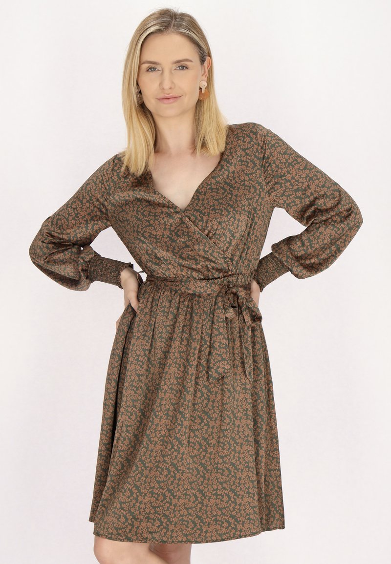 Wickeldress aus dunkelgrünem Stoff mit einem floralem Muster in Braun. Hat einen V-Ausschnitt, lange Ärmel und einen Bindegürtel in der Taille.