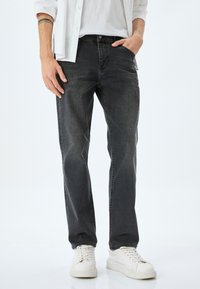 Jeans de mezclilla gris oscuro con corte recto, un ligero desgaste, diseño de cinco bolsillos y combinados con zapatillas blancas.