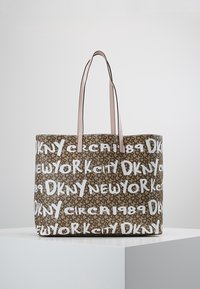Sac fourre-tout marron avec des poignées rose pâle, arborant un texte en style graffiti blanc "DKNY New York City circa 1989" sur un fond à motifs.