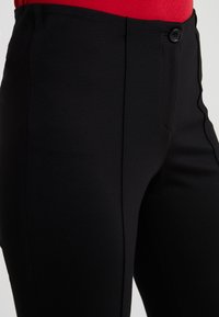 Pantalon noir avec une texture lisse, doté d'une fermeture à boutons à l'avant et de poches latérales, conçu avec des jambes droites.