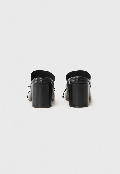 Svarta läder skor med blockklack, rund tå och öppen bak. Har en slät yta och minimalistisk design.