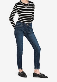 Raitapintainen mustavalkoinen ribattupusero, kapeat tummansiniset farkut, joissa on revennyt helma, sekä mustat loafersit tupsuyksityiskohdilla.