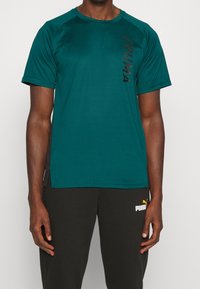 Tyrkysové sportovní tričko s krátkým rukávem, kulatým výstřihem a černým logem Puma na levé straně. Hladká, lehká tkanina s volným střihem.