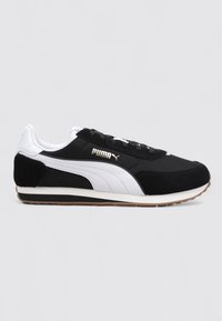 Czarno-białe sneakersy Puma z białym paskiem po bokach, złotym logo Puma, czarnymi sznurówkami i brązową gumową podeszwą na neutralnym tle.