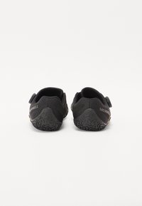 Fekete slip-on cipők texturált felsőrésszel, rugalmas oldalszíjakkal és tartós gumitalppal, amely tapadómintákkal rendelkezik. A saroknál "Merrell" felirat látható.