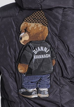 Crna topla jakna s teksturiranim patch-om medvjeda koji nosi crnu majicu s natpisom "GIANNI KAVANAGH" na leđima i plavim trapericama.