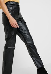 Black leather pants with a smooth texture, featuring side zipper pockets and rectangular patch pockets, tailored for a fitted silhouette.