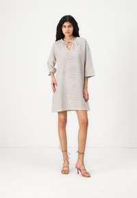 Vestido xadrez em bege claro com decote redondo, detalhe em forma de chave e mangas três quartos, combinado com sandálias de tiras em tom de areia.