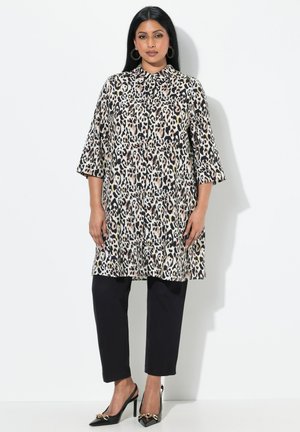 Leopardprint tunika med trekvartærmer og krave, parret med sorte bukser og spidse hæle med sløjfedetaljer.