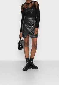 Haut noir à manches longues côtelé avec des détails transparents et des sequins, associ é à une jupe portefeuille en cuir noir avec des boutons décoratifs et une longueur mini.