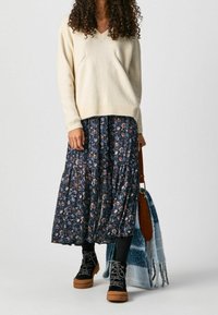 Cream v-neck sweater, floral navy maxi skirt, black lace-up boots with tan soles, and a brown handbag with a blue patterned scarf.