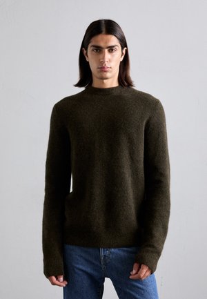 Dunkelgrüner Wollpullover mit Rundhalsausschnitt, langen Ärmeln und gerippten Bündchen, kombiniert mit blauen Jeans. Weicher, strukturierten Stoff.