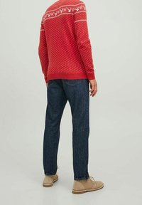 Rot gestrickter Pullover mit weißem Rentiermuster, kombiniert mit blauen Jeans und beigen Schuhen. Der Pullover hat einen gerippten Saum und Bündchen.