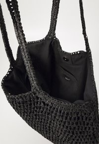 Czarna, pleciona torba na zakupy z mocnymi uchwytami. Wnętrze z gładką, czarną podszewką i małą kieszonką. Wyróżniająca się tekstura i lekka konstrukcja.