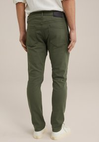 Olivgröna byxor i bomullsblandning, med två bakfickor med rundad sömnad, slim fit-design, i kombination med vita sneakers.