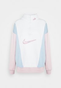 Sweat-shirt blanc avec un col zippé, panneaux bleu clair et rose, arborant un logo Nike en strass rose sur le devant. Texture douce, design décontracté.