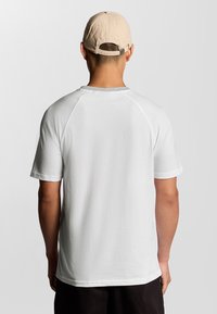 T-shirt bianco a maniche corte con maniche raglan. Tessuto morbido con scollatura rotonda. Berretto beige indossato all'indietro, con logo ricamato.