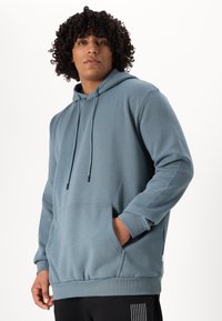 Hooded sweatshirt in soft blue fabric, featuring a front pocket, drawstring, and ribbed cuffs with a fitted hem.
