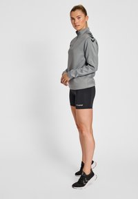 Grå zip-up sweatshirt med svarta chevron-accenter, svarta shorts med logotyp och svarta träningsskor. Slät tyg med en figurnära design.