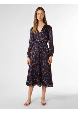 Blumendruckkleid in Schwarz mit blauen und roten Blumen, langen Ärmeln, V-Ausschnitt, taillierter Taille und ausgestelltem Saum. Kombiniert mit pinkfarbenen Slidesandalen.