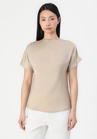 Haut beige à manches courtes avec un col bateau et un tissu lisse et léger. Présente une coupe décontractée et un léger éclat.
